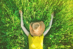 A person in a yellow t shirt lying on green grass with a hat covering their face