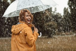 Redhead woman smiling looking at the camera holding an umbrella as it rains