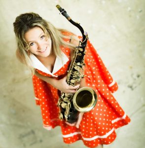 A woman in holding a saxophone looking into the camera